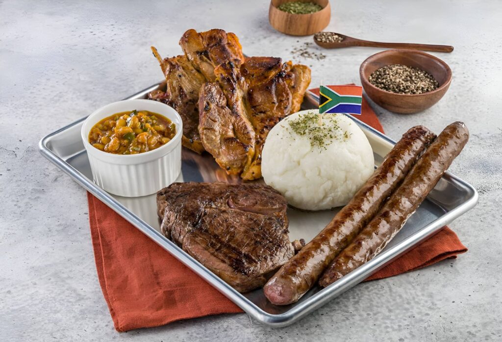 South African platter with grilled steak, boerewors sausage, chicken, pap, and chakalaka served on a tray with traditional flavors.