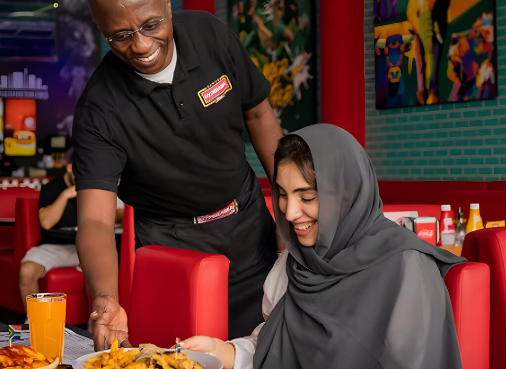 Server presenting a traditional South African meal to a diner at Hyperama Diner in Dubai