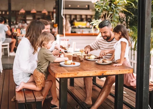 Family with young children enjoying a relaxed outdoor brunch at a kid-friendly restaurant in Dubai, with pancakes and shared plates on a wooden table.