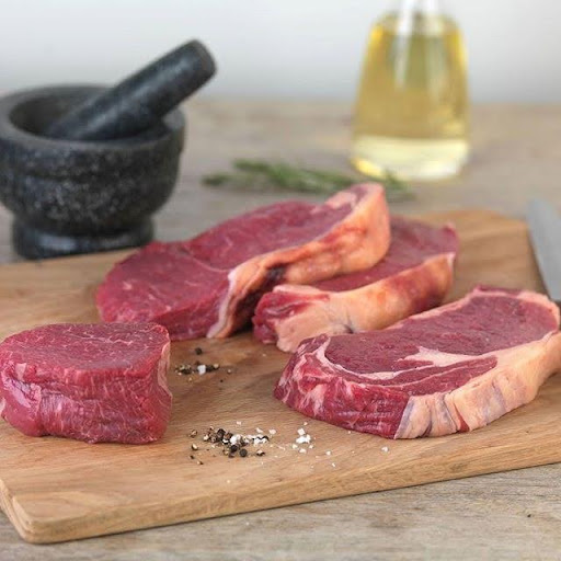 Raw ribeye and sirloin steak cuts on a wooden board with mortar and pestle, rosemary, and olive oil