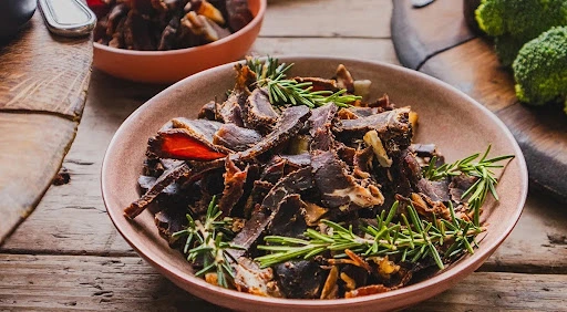 Sliced South African biltong garnished with fresh rosemary, served in a bowl on a wooden table