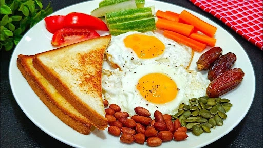 Breakfast plate with fried eggs, toast, sliced vegetables, dates, peanuts, and pumpkin seeds.