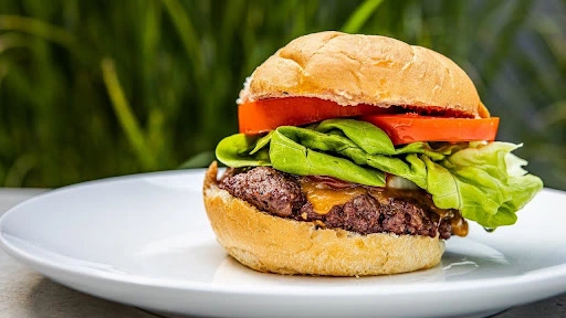 Medium-rare beef burger with lettuce, tomato, and melted cheese served on a white plate.