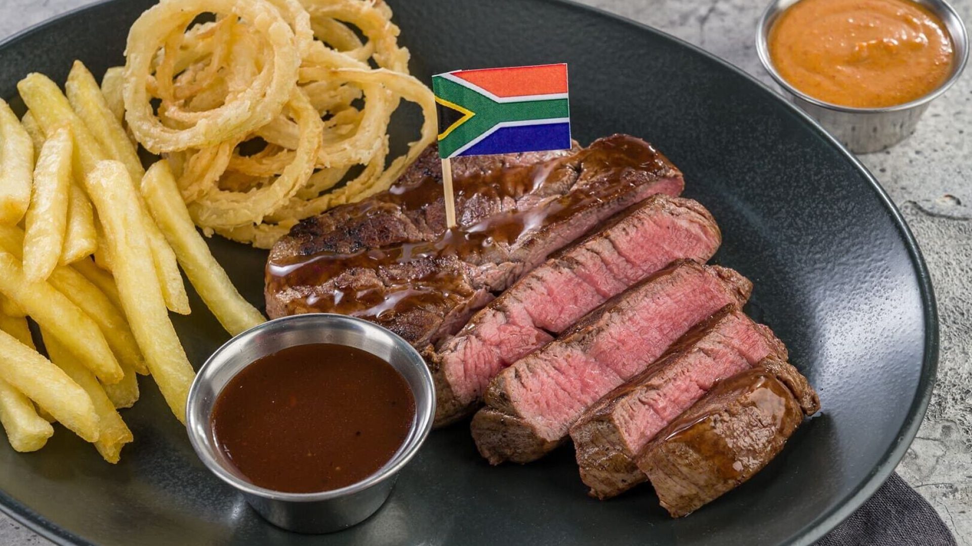 Hyperama steak plate with sliced beef, fries, onion rings, and sauces.