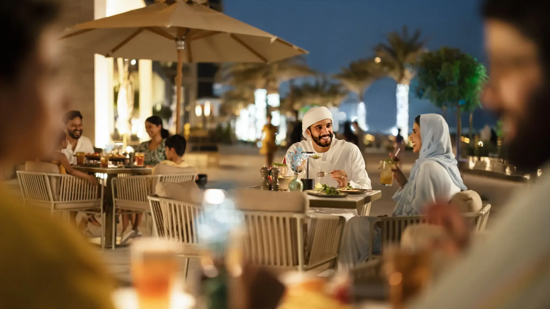 Diners enjoying an evening meal at an outdoor restaurant terrace in Abu Dhabi, capturing the city's vibrant al fresco dining scene.