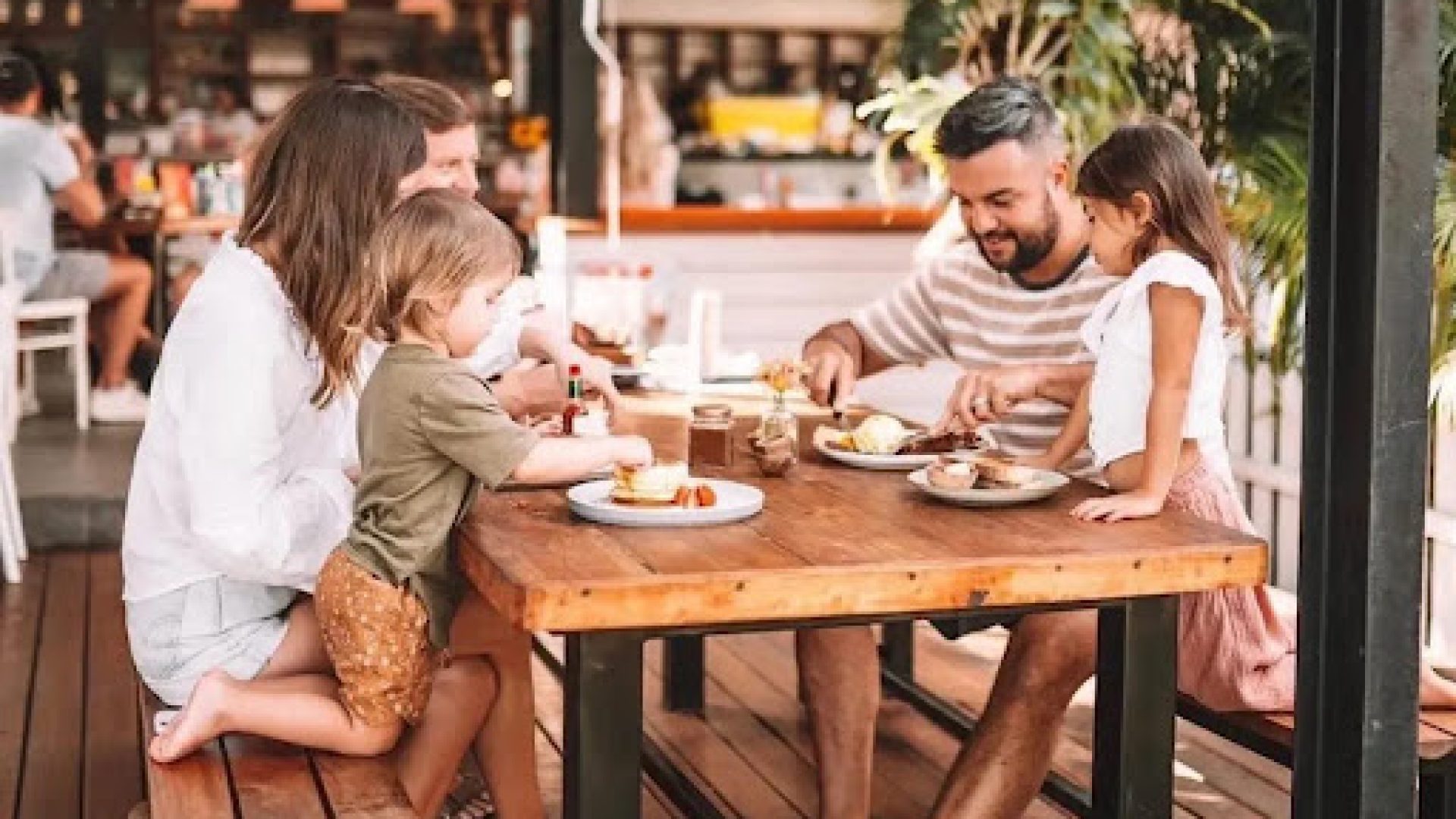 Family with young children enjoying a relaxed outdoor brunch at a kid-friendly restaurant in Dubai, with pancakes and shared plates on a wooden table.