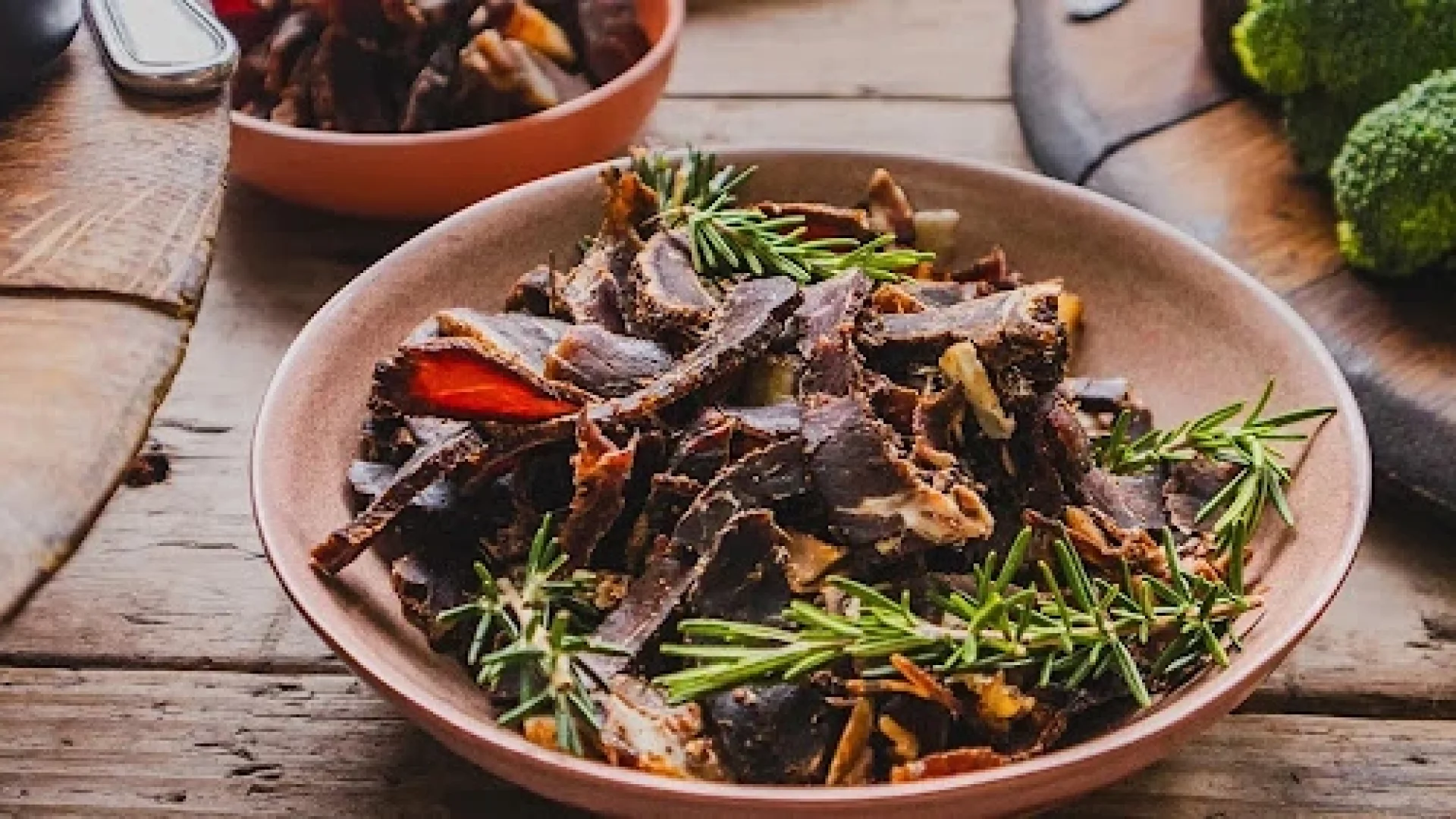 Sliced South African biltong garnished with fresh rosemary, served in a bowl on a wooden table